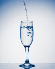 Water pouring into champagne glass with splashes on white background