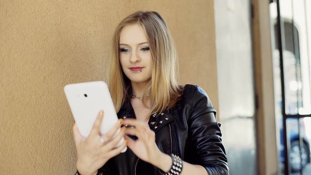 Punk girl standing next to the wall and browsing internet on tablet
