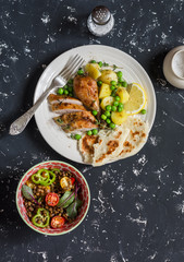 Lemon thyme baked chicken, boiled potatoes with green peas, salad with lentils and tomatoes on a dark background. Top view