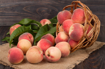 peaches in a wicker basket with leaves on wooden table