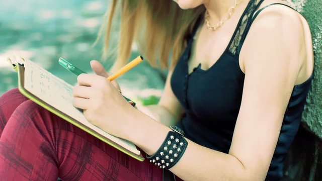 Punk girl making notes in her journal and checking information on smartphone
