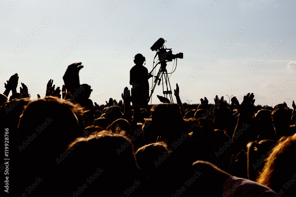 Wall mural silhouette of cameraman operator shooting a live rock concert, fans around raised hands