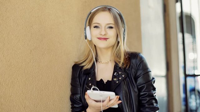 Punk girl listening music on headphones and smiling to the camera

