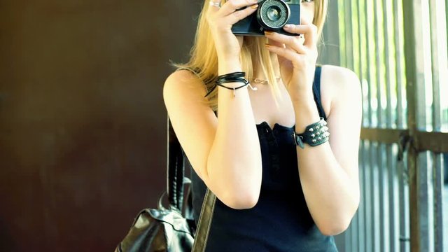 Punk girl standing next to the gate and doing photos on old camera, steadycam shot
