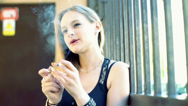 Punk girl fire the cigarette and smoking it next to the gate
