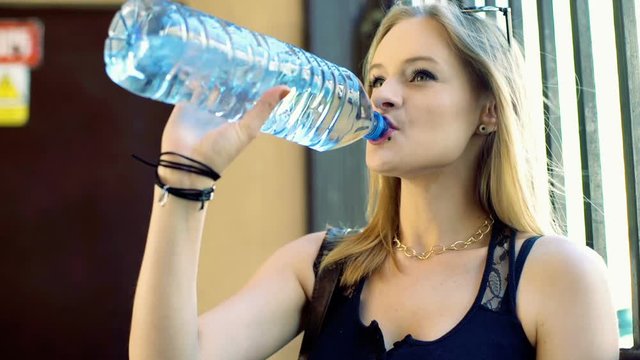 Pretty, punk girl standing next to the gate and drinking water

