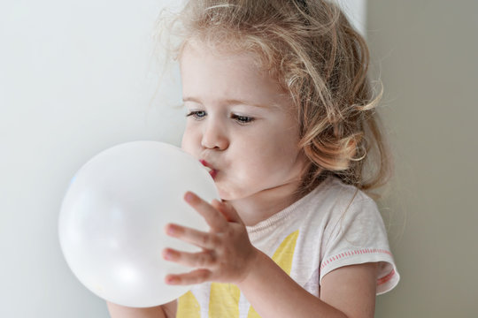 Adorable child girl is inflating a white balloon close-up