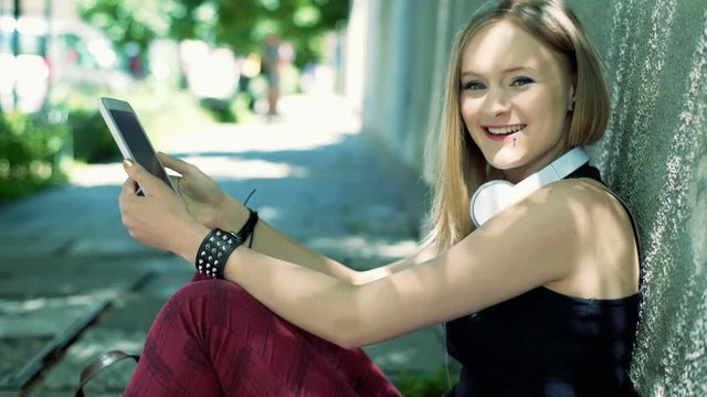 Punk girl sitting on a pathway and smiling to the camera
