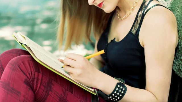 Angry, punk girl sitting on pathway and crossing something out from notebook
