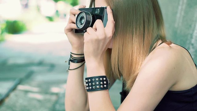 Punk girl sitting on the pathway and doing photos on old camera, steadycam shot
