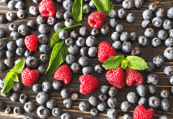 Blueberries, raspberries and mint at black wooden table.