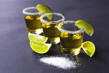 Gold tequila with lime and salt on dark table