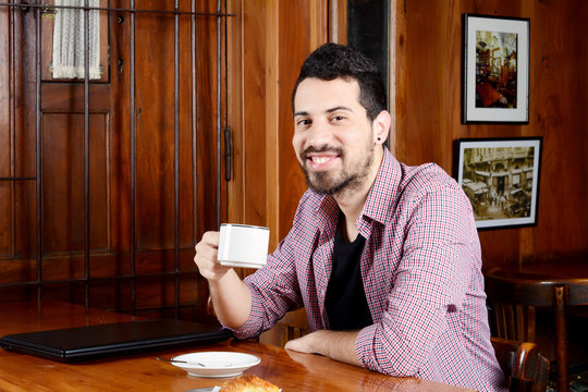 Young latin man drinking coffee at a cafe.