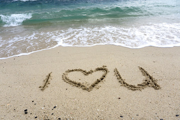 Fototapeta na wymiar I love you words and shape on a sand beach with sea waves