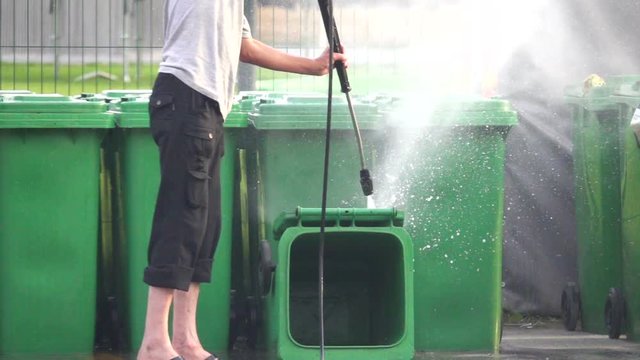 Cleaner cleans plastic dumpster with water from a hose under pressure, slow motion