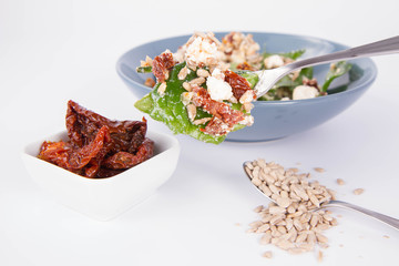 Spinach, dried tomatoes, feta cheese and sunflower seeds salad being eaten with a fork