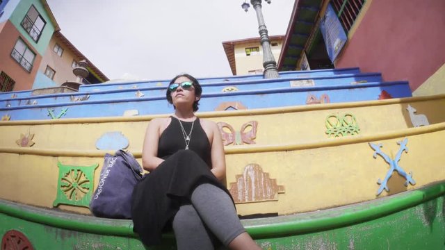 Colombian Woman seated on the stairs of the Plaza de los Zocalos, Guatape, Colombia. 4k