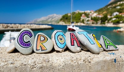 Croatia name painted on the stones, boat in marina in background - obrazy, fototapety, plakaty