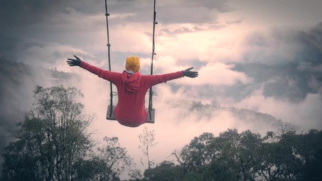 Woman over swing that elevates to the sky, open arms feeling the freedom pf flying on a foggy day at the tree house, Ba&ntilde;os Ecuador. 