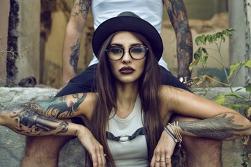 Gorgeous tattooed girl with provocative make up sitting between her boyfriend's legs in the ruined...