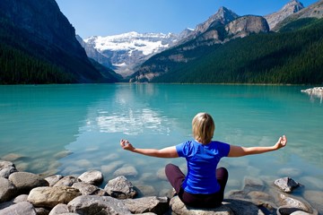 Fototapeta na wymiar Woman in yoga pose meditating by water. Lake Louise in Canadian Rockies. Banff National Park. Alberta. Canada. 
