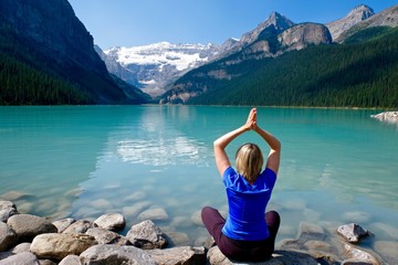Woman in yoga pose meditating by water.