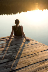 Relaxing young woman in nature. Sunlight on water.