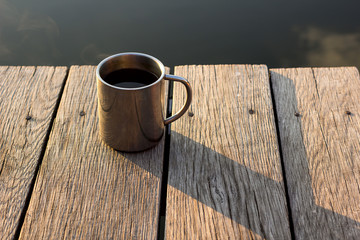 Thermo cup with coffee on old wooden pier.