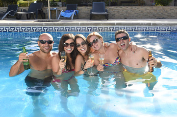 happy attractive men and women in bikini having bath at hotel resort swimming pool drinking beer