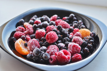 A plate of fresh frozen berries including raspberry, black current, and apricots