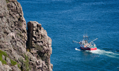 Bright red fishing boat heads out to sea on sunny summer day from St. John's harbor Newfoundland, Canada.
