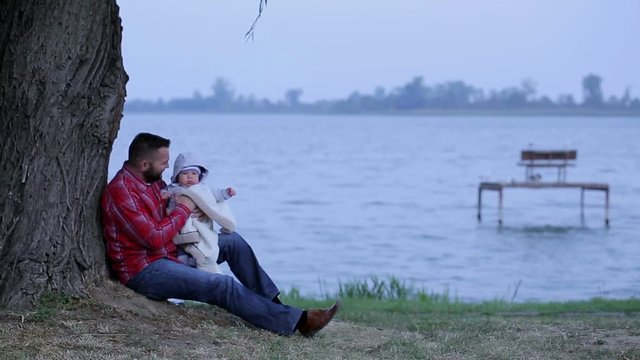 Father with little son is sitting near lake

