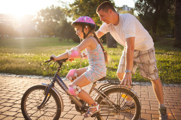 Fototapeta na wymiar Girl learning to ride a bicycle with father in park