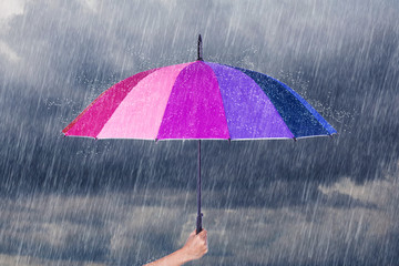 hand holding multicolored umbrella under dark sky with rain