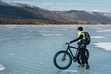 Obraz premium Fatbike (also called fat bike or fat-tire bike) - Cycling on large wheels. Cyclist holding a bike, and watching the sunset. They are standing on the frozen lake.