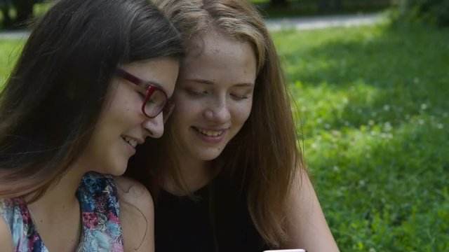 Happy teenger girls with mobile phone in the park. Friends laughing when looking at photos or browsing web
