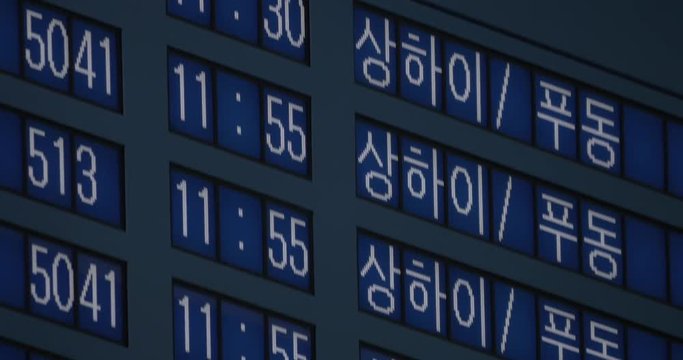Close-up tilt shot of international arrivals on flight schedule with information on Korean and English languages