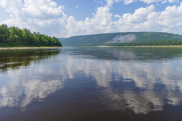 Summer day landscape with river, cloudy sky and forest. 