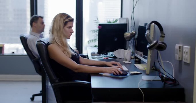 Business woman working diligently at computer in creative open-plan city office. Disruptive male co-worker fires toy gun behind her.  Wide shot, recorded in real time with other workers.