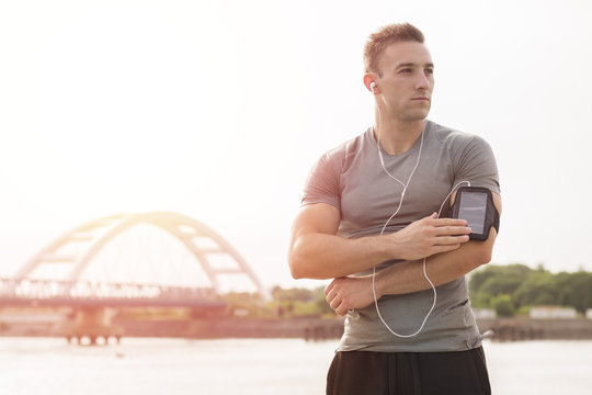 Running training music - runner man listening to music adjusting settings on armband for smartphone.