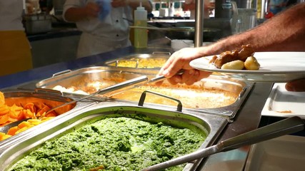 Buffet food indoor in restaurant with meat, potato, spinach, carrots, and other vegetables