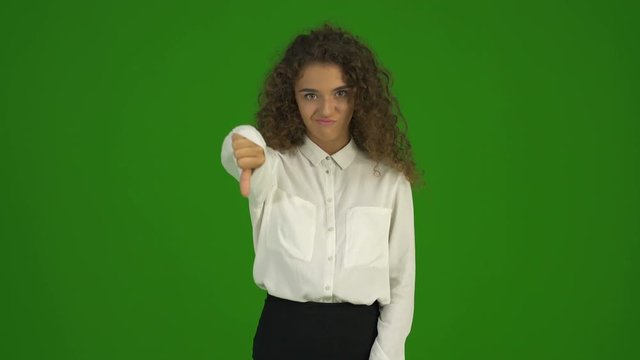 The curly businesswoman thumb down and stand on the green background. Real time