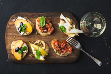 Bruschetta set with glass of white wine. Black plywood background, top view, horizontal composition