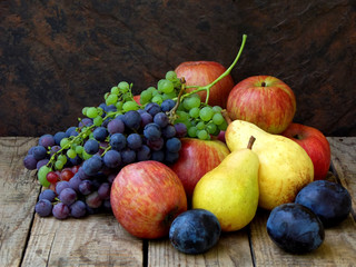 still life of autumn fruits: grapes, apples, pear, plum on a wooden background. selective focus
