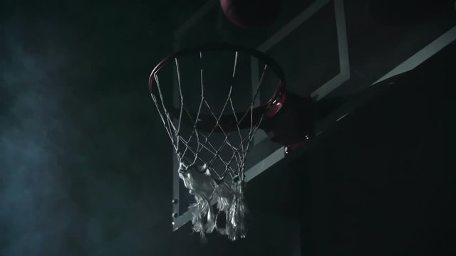 Slow motion shot of ball balancing on rim before falling through the basketball net at night