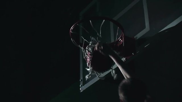 Slow motion shot of basketball player putting the ball directly through the basket with one hand in the darkness