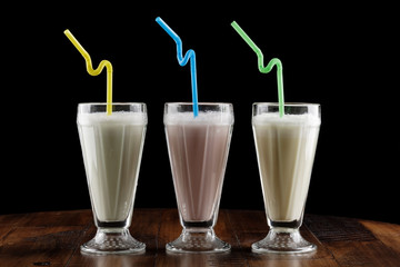 Milk shake (cocktail) with berry and banana in glass on brown wooden table