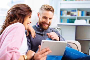 Happy couple browsing internet on digital tablet sitting togethe