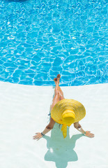 beautiful woman in a hat sitting on the edge of the pool