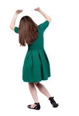back view of woman protects hands from what is falling from above. Slim brunette woman in green short dress holds something over his head.